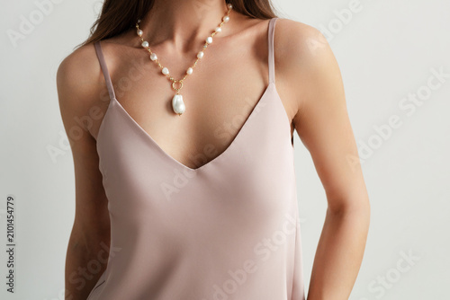 Obraz na plátne Woman wearing a pastel pink silk camisole and a gold chain necklace featuring a large pearl pendant, faceless shot