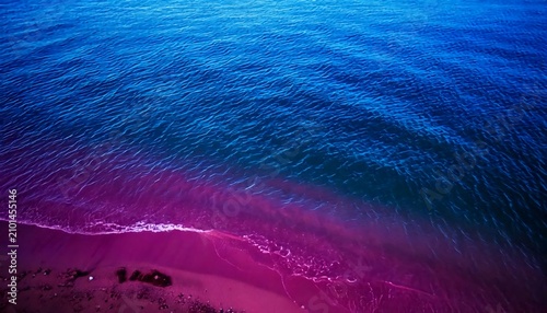 Vibrant purple beach meets deep blue sea waves in aerial view