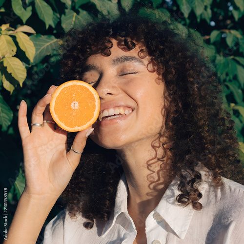 Happy Woman Holding Fresh Orange Slice in Tropical Nature Setting