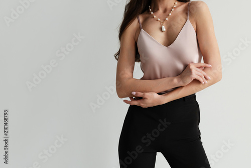 Photography A faceless woman in a pink silk camisole and black trousers wearing a gold chain pearl necklace, with blank copyspace on the left