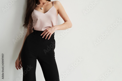 Foto A faceless woman wearing a pink satin camisole and high-waisted black trousers on a light background with empty copyspace on the right