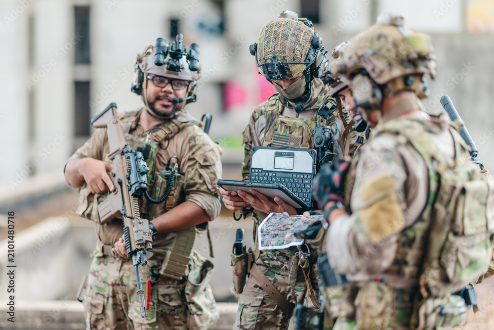 Fototapeta premium Military tactical team reviews mission plan on rugged laptop during outdoor field briefing