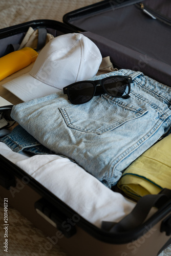 Open suitcase packed with summer clothes, sunglasses and travel essentials ready for vacation.