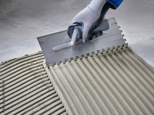Professional tiler applying adhesive, notched trowel spreading mortar on floor