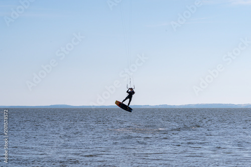 фотографія Professional kitesurfer jumps high into the bright blue sky above the rippling o
