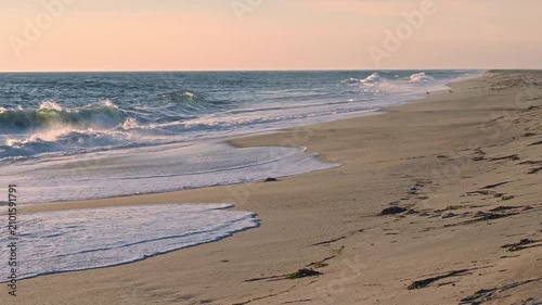 Gentle ocean waves roll onto the sandy beach as the warm golden light of the setting sun reflects beautifully across the water’s surface