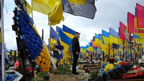 Cuadro en lienzo Mourning man standing among countless graves of ukrainian soldiers with national banners pay tribute to fallen family member in Kharkiv