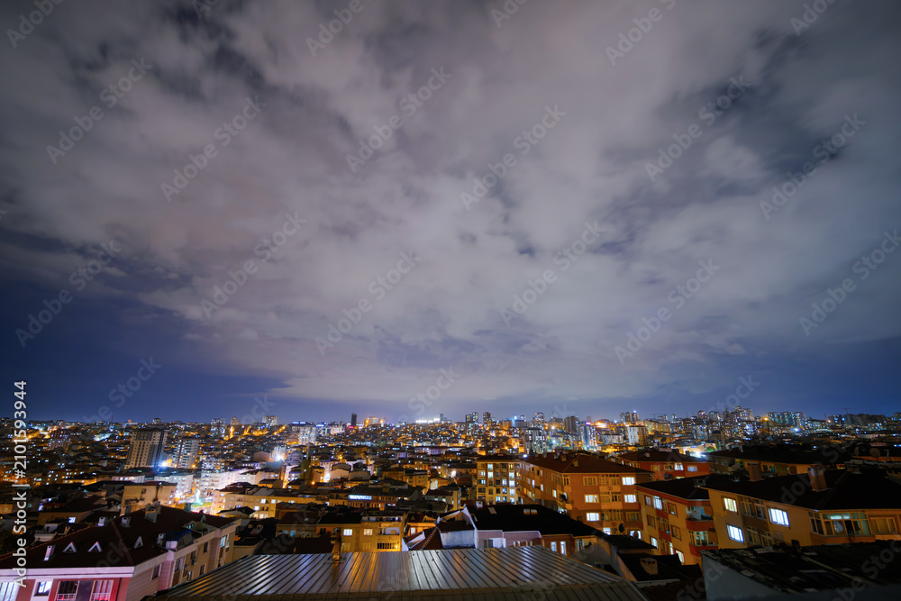 Fototapeta premium Clouds in the dark sky over cityscape with turkish apartment, residential buildings with warm lighting and illuminated windows in Istanbul, Turkey at night: wide angle