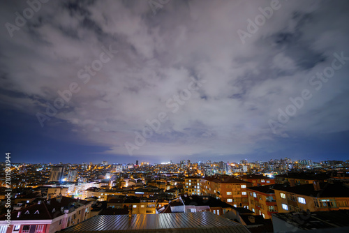 Clouds in the dark sky over cityscape with turkish apartment, residential buildings with warm lighting and illuminated windows in Istanbul, Turkey at night: wide angle