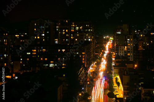 Dark street, road with many fast moving cars with headlights on at night - light trails, high contrast, long exposure. Urban, city traffic and transportation concept