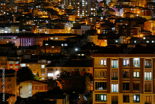 View of the roofs, rooftops of typical turkish multistory residential buildings with illuminated windows and warm street lighting in Istanbul, Turkey at night. Architecture concept
