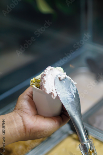 Close-up of artisan gelato being freshly served into a white paper cup using a metal scoop. Premium dessert preparation with shallow depth of field for hospitality and food marketing.