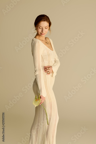 Mature woman in elegant fashion poses gracefully with a flower in a soft, serene setting