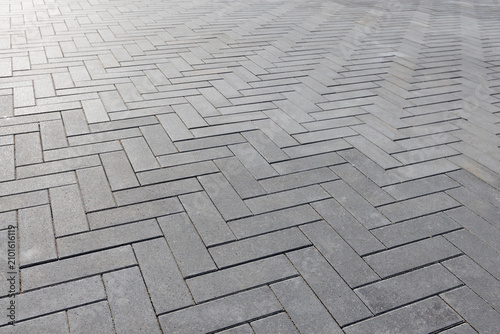 Gray concrete pavers forming a clean Herringbone geometric pattern of an outdoor walkway. Close-up view emphasizes texture  repetition and modern design for urban pathways. Selective focus