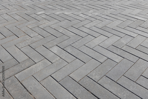 Herringbone pattern of gray concrete pavers forming a clean  geometric outdoor walkway. Close-up view emphasizes texture  repetition and modern hardscape design for urban pathways