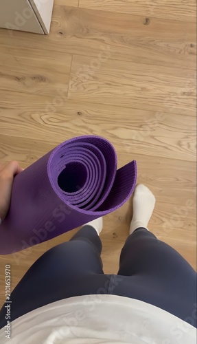 Authentic lifestyle photo capturing a person holding a purple yoga mat indoors with natural daylight. A genuine wellness, fitness, and home exercise moment, photographed with a real camera for commerc