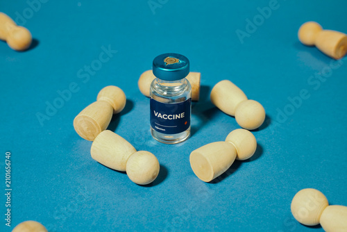 Vaccine vial surrounded by wooden human figures on blue background