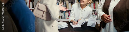 Fotografie Header of Caucasian young woman signing book while greeting readers at bookstore event, promoting author branding and publishing