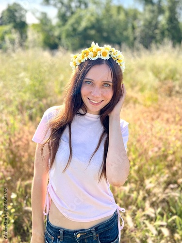 Happy beautiful young woman is smiling in the field with wreath of daisy flowers on the head