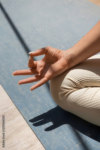 Authentic close-up of a hand practicing a meditation mudra on a yoga mat in warm natural sunlight. Real lifestyle wellness moment with soft shadows, mindful balance, relaxation, and healthy living.
