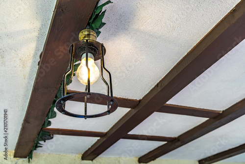 A man replaces a burned-out light bulb in a fixture on a porch in front of a house in the garden, unscrewing and screwing in a burned-out LED bulb in a lamp hanging from the ceiling 