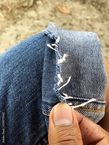 Fotografie Close up of a hand holding frayed blue denim jeans with loose white threads