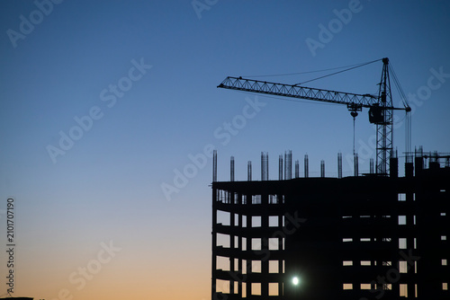 Silhouette of a building under construction with cranes at sunset
