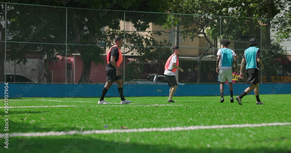 Fototapeta premium Group of friends enjoying casual soccer match on local field, players in colored vests running and passing ball, concept of teamwork, energy, and social recreation