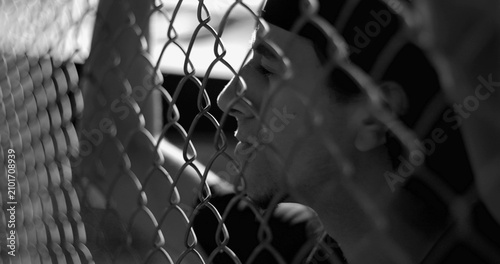 Bild auf Leinwand Hispanic man behind fence lost in ruminating thoughts, reflecting on past mistak