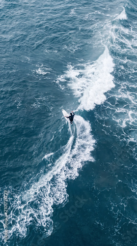 Aerial view of a lone surfer carving a foaming wake across deep blue ocean