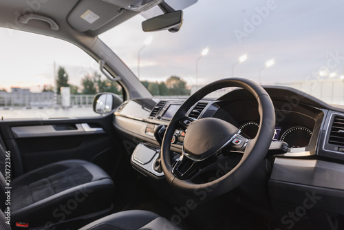 Right-hand drive van interior with cloth seats. Minivan cockpit wide angle view from drivers side: seats, steering wheel, dashboard and center console.