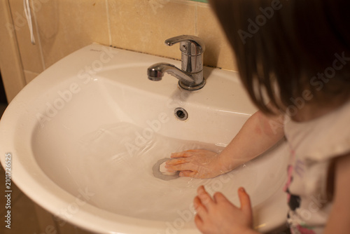 Fotografie Child washing hands with soapy cloth at sink, visible lather and careful rubbing