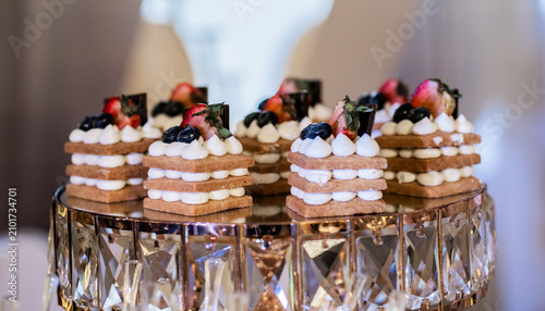 Mini postres gourmet con crema, fresas y arándanos sobre elegante soporte de cristal para eventos
