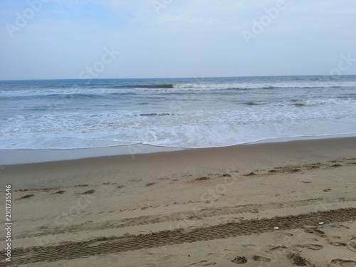 Billede på lærred Scenic coastal view of ocean waves hitting a sandy beach with tire treads seasca