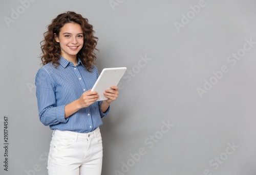 Smiling young woman holding a tablet in a casual office setting with gray background