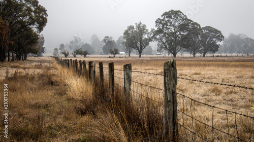 Rustic wooden fence with barbed wire in a foggy rural landscape on a cold misty morning in the countryside
