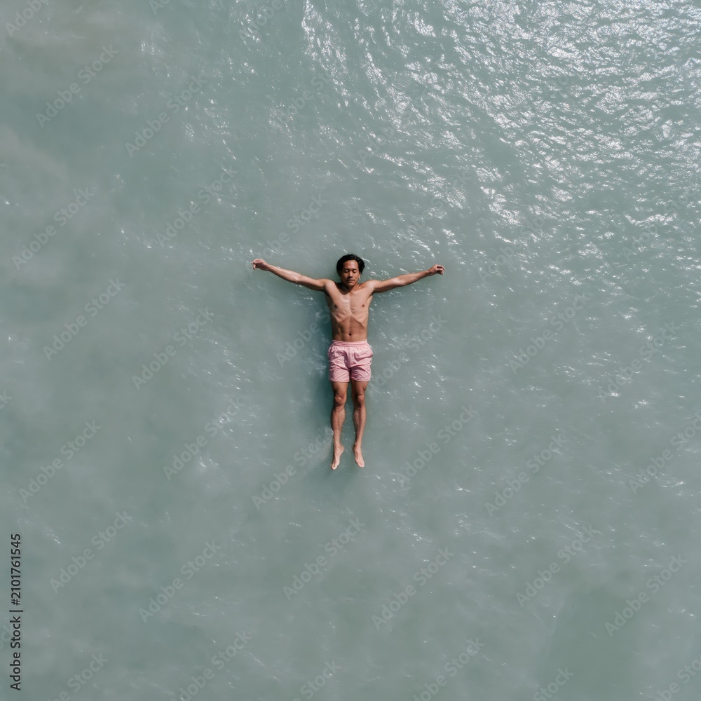 Fototapeta premium Aerial view of a man floating on calm turquoise water in pink swim shorts for summer relaxation background and wellness banner