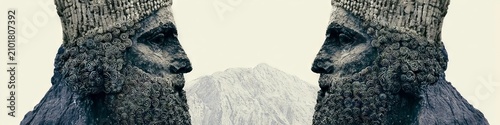 Two colossal royal heads in profile form a symmetrical gateway, their bearded faces and crowns crafted from spiraling stone patterns, framing a distant mountain horizon under a pale sky.