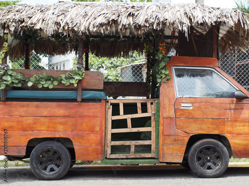 Exotic Caribbean vehicle on a street, designed with wooden elements and topped with thatch. It has plants and flowers decorating its sides. This scene captures local transport culture. 