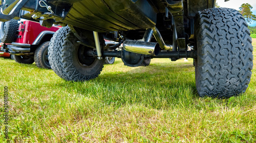 Fotografie Underbody view of a lifted off-road truck showing suspension, exhaust pipe, and large tires on grass