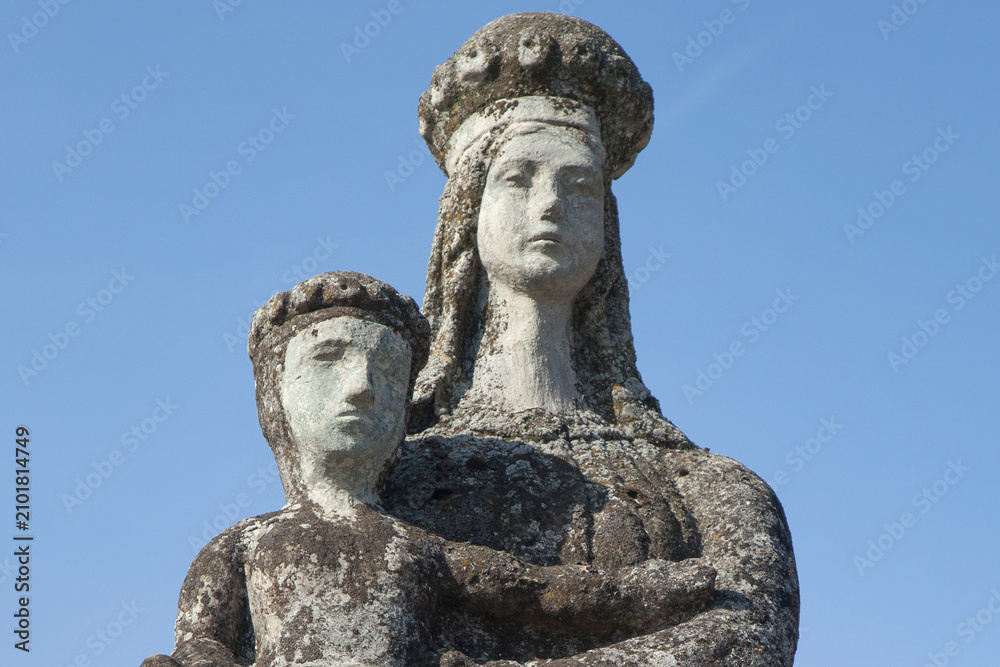 Obraz premium Weathered stone statue of the crowned Virgin Mary holding the Christ Child beneath a clear blue sky.