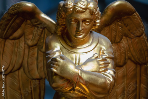 Canvastavla Elegant golden guardian angel statue with folded arms and detailed wings, symbolizing divine protection, peace, comfort, hope, and heavenly grace in warm light