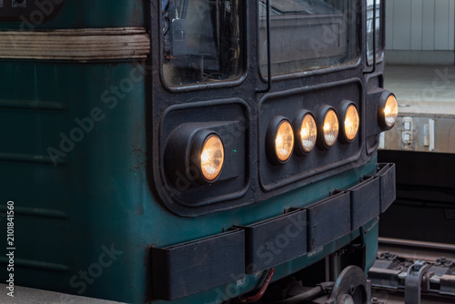 Photos Front view of old green train locomotive with glowing yellow headlights in depot