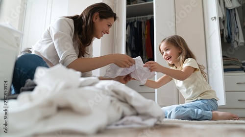 Mother and daughter smiling while folding clean laundry, teaching chores and responsibility, working together, bonding at home, enjoying daily housework