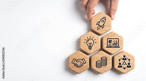 A hand places a hexagonal wooden block with a rocket icon on top of a pyramid of business concept blocks, symbolizing startup growth and strategic development.