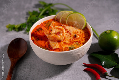 Spicy Thai seafood soup served in a white bowl with shrimp, squid, lime, chili, and fresh herbs on a wooden table, traditional Asian cuisine concept.