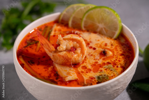Spicy Thai seafood soup served in a white bowl with shrimp, squid, lime, chili, and fresh herbs on a wooden table, traditional Asian cuisine concept.