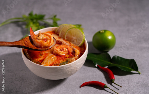 Spicy Thai seafood soup served in a white bowl with shrimp, squid, lime, chili, and fresh herbs on a wooden table, traditional Asian cuisine concept.