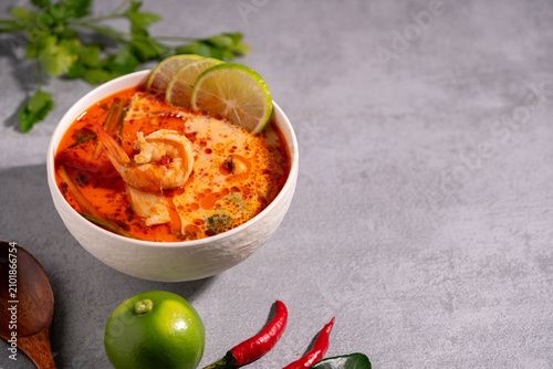 Spicy Thai seafood soup served in a white bowl with shrimp, squid, lime, chili, and fresh herbs on a wooden table, traditional Asian cuisine concept.