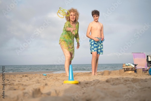 Mother and son playing ring toss game together on a sandy beach during a cloudy autumn day by the sea